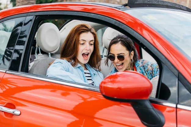 Überraschte junge Dame und fröhliche Frau, die im Auto sitzt