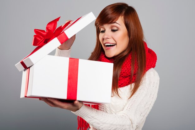 Überraschte junge Frau, die in das Weihnachtsgeschenk späht