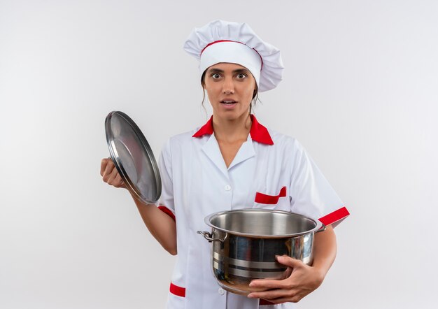 Überraschte junge Köchin, die Kochuniform trägt, die Topf und Deckel mit Kopienraum hält