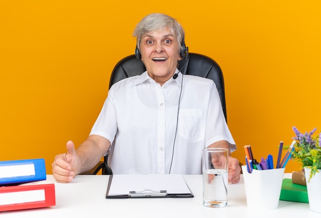 Überraschte kaukasische Callcenter-Betreiberin mit Kopfhörern, die mit Bürowerkzeugen am Schreibtisch sitzen