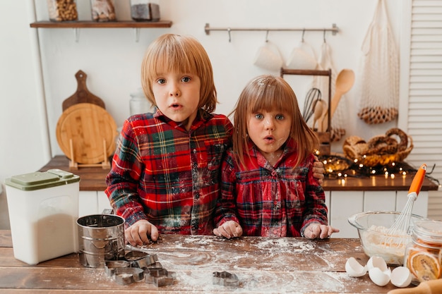 Überraschte Kinder, die zusammen Weihnachtsplätzchen machen