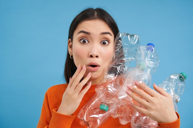 Überraschte koreanische Frau hält Plastikflaschen in der Hand und blickt schockiert auf das Kamerakonzept der Umwelt und
