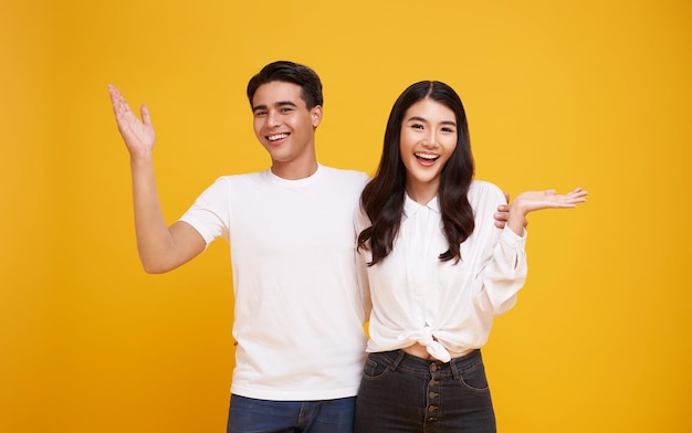 Überraschtes asiatisches Paar steht lächelnd da und öffnet die Hände, isoliert auf gelbem Studiohintergrund