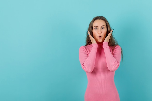 Überraschtes blondes Mädchen hält Hände um Gesicht auf blauem Hintergrund