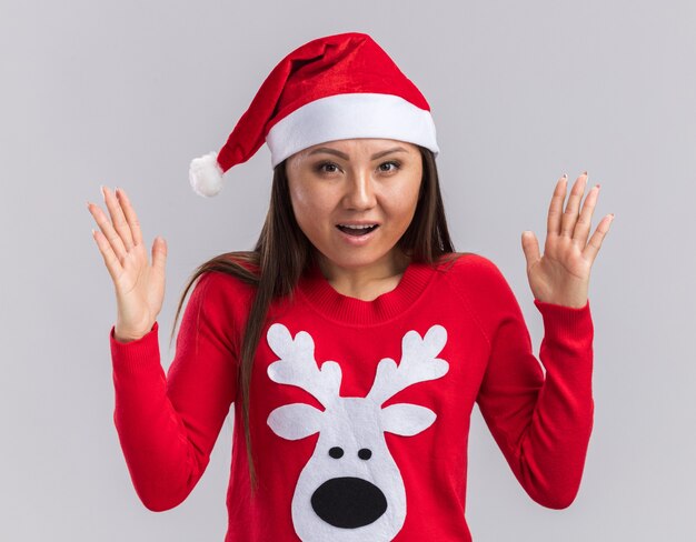 Überraschtes junges asiatisches Mädchen, das Weihnachtsmütze mit Pullover trägt Größe zeigt, die auf weißem Hintergrund lokalisiert wird