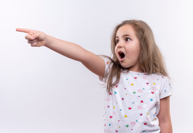 Überraschtes kleines Schulmädchen, das weiße T-Shirt-Punkte an der Seite auf lokalisiertem weißem Hintergrund trägt