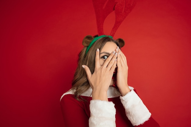 Überraschtes verstecktes Gesicht. Konzept von Weihnachten, Neujahr, Winterstimmung, Feiertagen. . Schöne kaukasische Frau mit langen Haaren wie Santa's Rentier anziehende Geschenkbox.