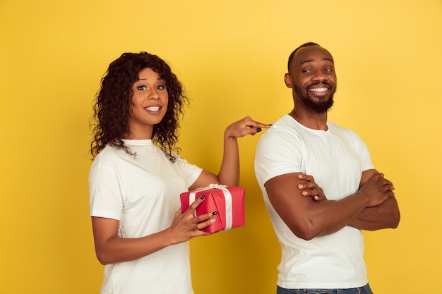 Überraschung geben. Valentinstagfeier, glückliches Afroamerikanerpaar lokalisiert auf gelbem Studiohintergrund. Konzept der menschlichen Gefühle, Gesichtsausdruck, Liebe, Beziehungen, romantische Feiertage.