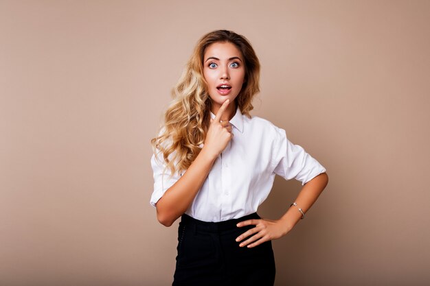 Überraschungsgesicht. Blonde Frau im lässigen Outfit, das über beige Wand steht. Aufgeregtes Mädchen suchen.