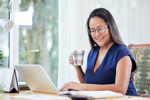 Überzeugte ethnische Geschäftsfrau mit Kaffee am Arbeitsplatz