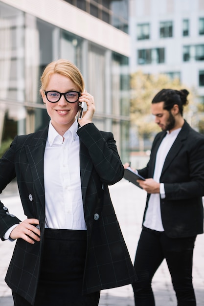 Überzeugte junge Geschäftsfrau, die am Handy mit ihrem Kollegen arbeitet am Hintergrund spricht