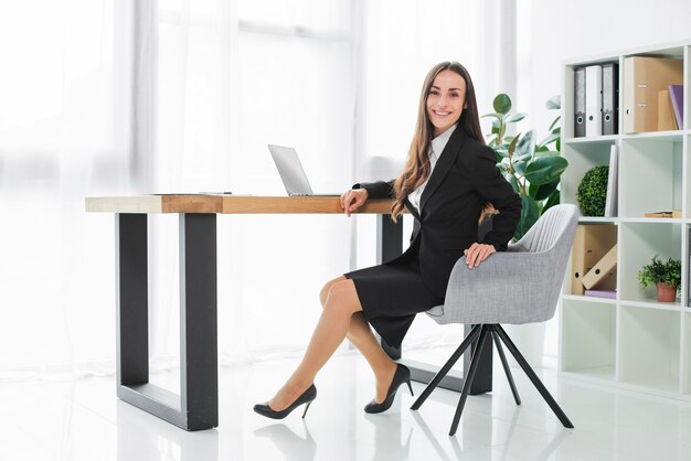 Überzeugte lächelnde junge Geschäftsfrau, die am Schreibtisch in ihrem modernen Büro sitzt