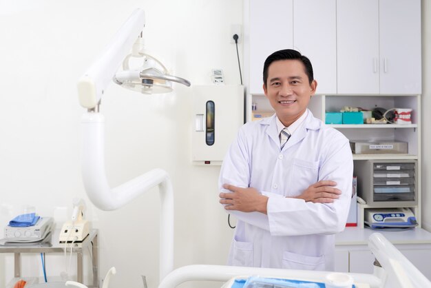 Überzeugter asiatischer männlicher Zahnarzt von mittlerem Alter, der in der Klinik aufwirft