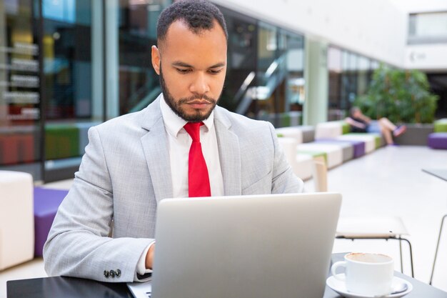 Überzeugter hübscher Unternehmensleiter, der Laptop verwendet