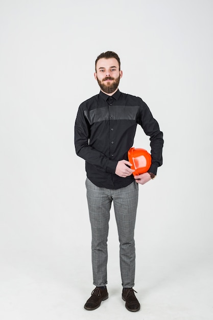 Überzeugter männlicher Architekt, der einen orange Hardhat gegen weißen Hintergrund hält