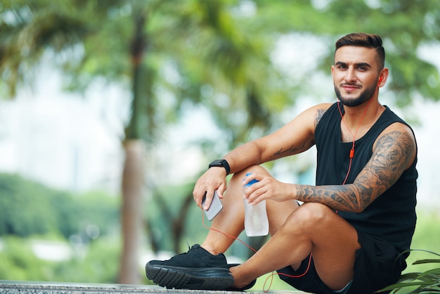 Überzeugter Sportler mit dem Telefon, das draußen sitzt