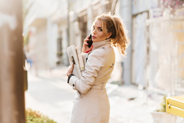 Beschäftigte Dame mit der trendigen Frisur, die über die Schulter schaut, während sie am Telefon spricht