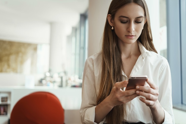 Beschäftigte erfolgreiche junge Geschäftsfrau, die Nachrichten auf Handy überprüft.