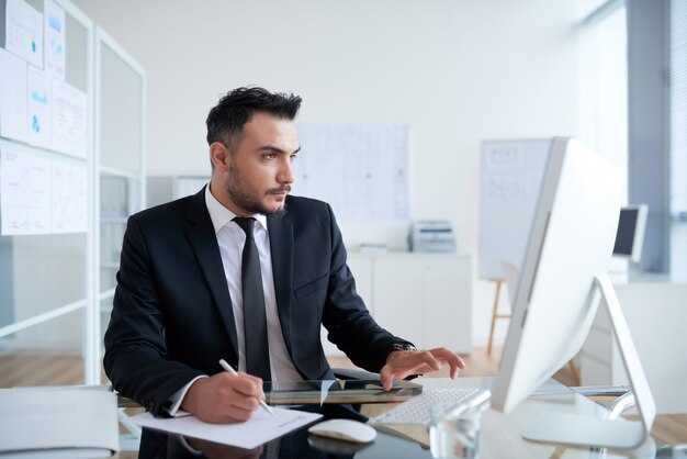 Beschäftigter kaukasischer Mann in der Klage, die im Büro sitzt und an Computer arbeitet
