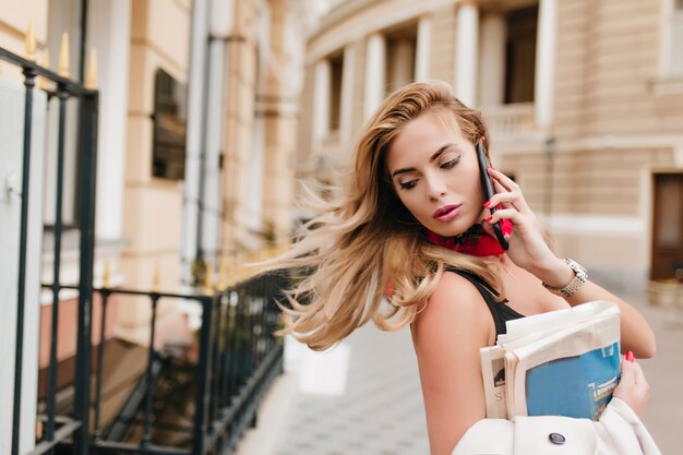 Beschäftigtes spektakuläres Mädchen mit blonden Haaren, die zum Büro eilen und am Telefon sprechen