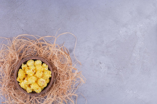 Bescheidene schüssel auf einem strohhaufen gefüllt mit mit süßigkeiten überzogenem popcorn auf marmorhintergrund. foto in hoher qualität