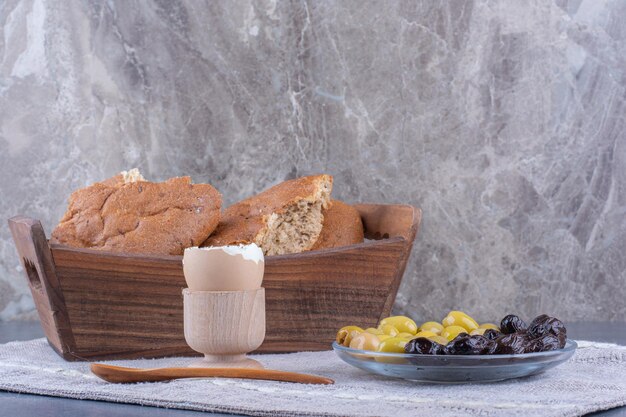 Bescheidenes Frühstücksset mit Brot, Ei und Oliven auf Marmoroberfläche