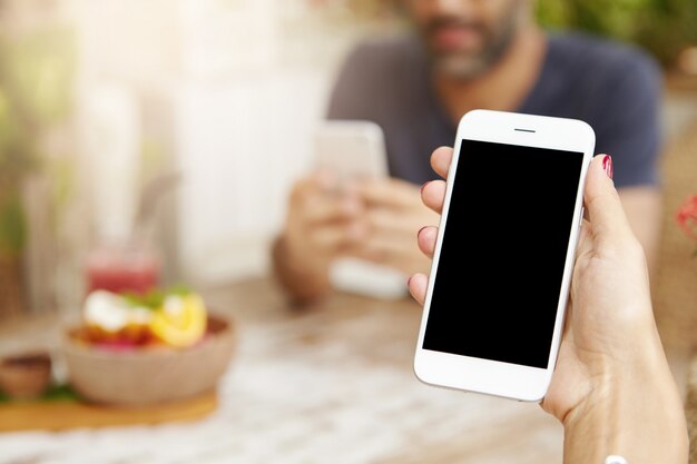 Beschnittene Ansicht der jungen Frau unter Verwendung des Touchscreen-Smartphones während des Mittagessens im Café