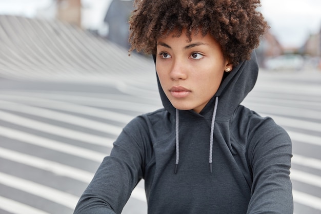 Beschnittene Ansicht der nachdenklichen dunkelhäutigen jungen Sportlerin im stilvollen Kapuzenpulli