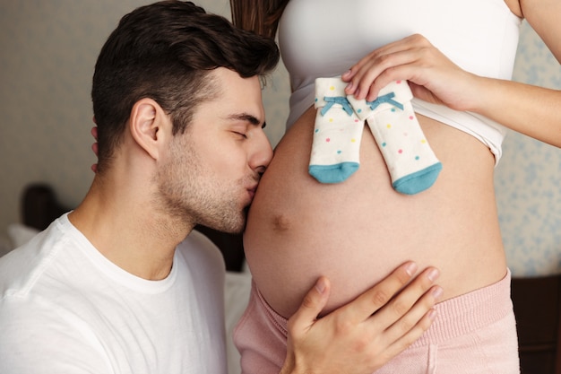 Beschnittenes Bild des Mannes, der Bauch seiner reizenden schwangeren Frau küsst