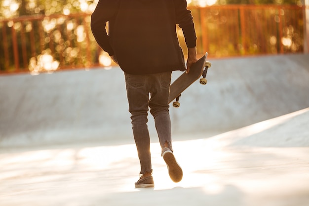 Beschnittenes Bild eines jungen afrikanischen Mannskateboarders, der geht