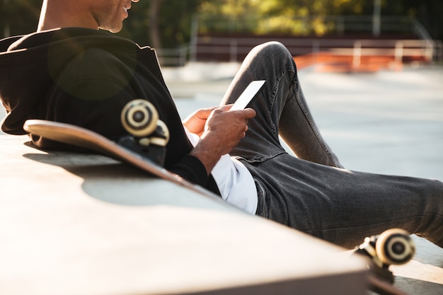 Beschnittenes Bild eines lächelnden Skateboarders, der Handy betrachtet