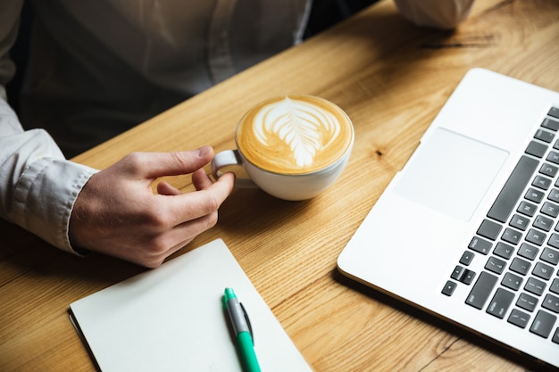 Beschnittenes Foto der Hand des Mannes im weißen Hemd, das Kaffeetasse hält