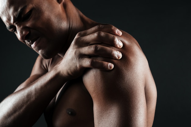 Beschnittenes Foto des jungen hemdlosen afroamerikanischen Mannes mit Schulterschmerzen