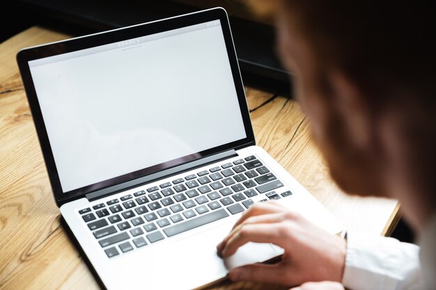 Beschnittenes Foto des jungen Mannes, der Laptop auf Holztisch verwendet