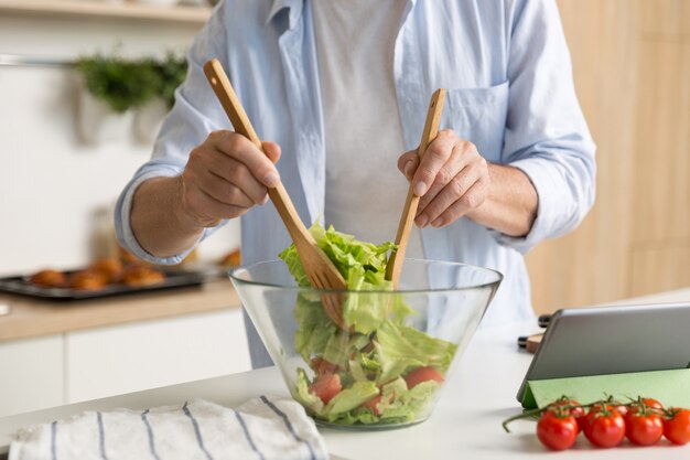 Beschnittenes Foto des reifen Mannes, der Salat kocht