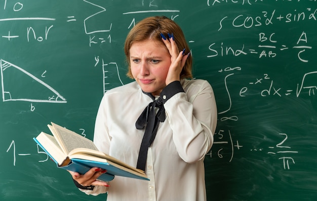 besorgte junge Lehrerin, die im Klassenzimmer vor der Tafel steht und ein Buch liest