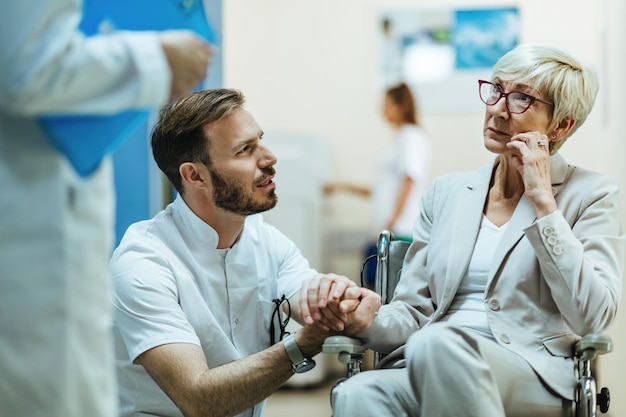 Besorgte reife Frau im Rollstuhl, die mit Ärzten in der medizinischen Klinik kommuniziert