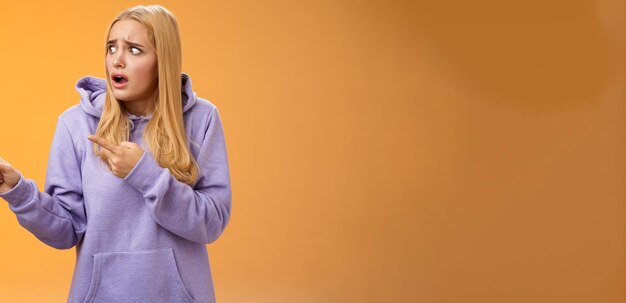 Kostenloses Foto besorgter freakout, der in panik gerät, lustiges blondes mädchen, das nach luft schnappt, die augen fallen lässt und nach links zeigt, schockiert und betäubt