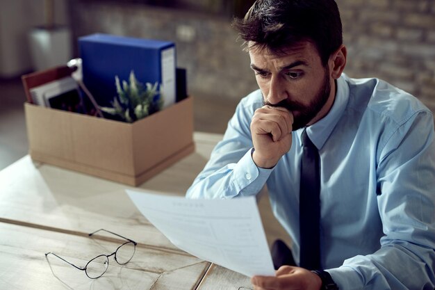 Besorgter Geschäftsmann, der Papierkram durchgeht, nachdem er seinen Job im Büro verloren hat