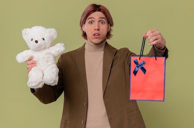 Besorgter junger gutaussehender Mann mit weißem Teddybär und Geschenktüte