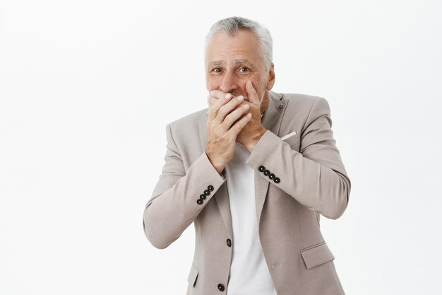 Besorgter und schockierter älterer Mann bedeckt den Mund mit den Händen und sieht besorgt aus