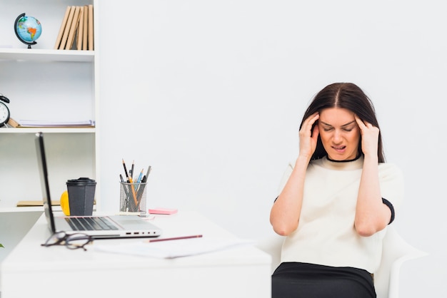 Betonte Frau, die am Tisch im Büro sitzt