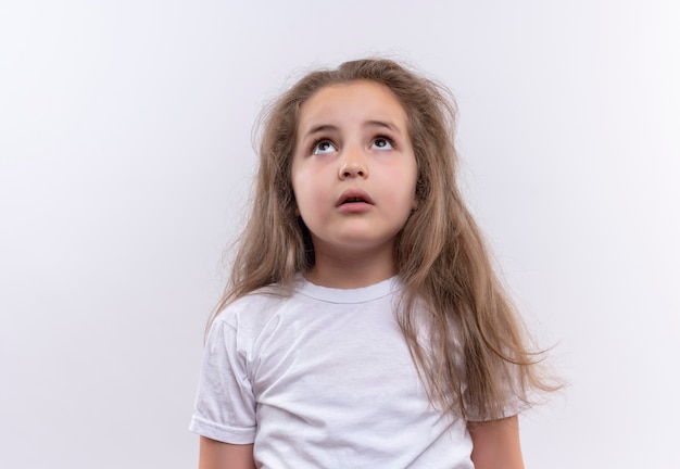 Betrachten des kleinen Schulmädchens, das weißes T-Shirt auf lokalem weißem Hintergrund trägt