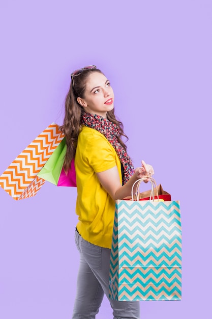 Kostenloses Foto betrachtung der frau, die einkaufstasche gegen purpurroten hintergrund hält