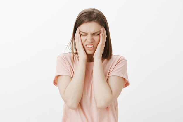 Betroffene junge Frau verzieht das Gesicht vor schmerzhaften Gefühlen, hat Migräne oder Kopfschmerzen
