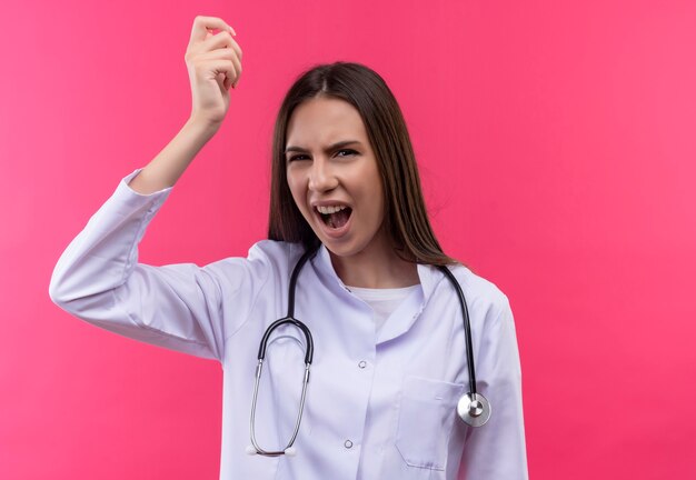 Betroffene junge Ärztin, die das medizinische Kleid des Stethoskops trägt, das Hand auf isolierter rosa Wand erhebt