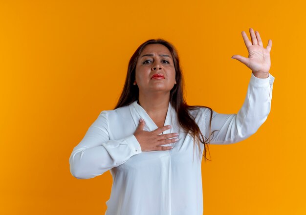 Betroffene zufällige kaukasische Frau mittleren Alters, die Hand hebt und andere Hand auf Herz legt