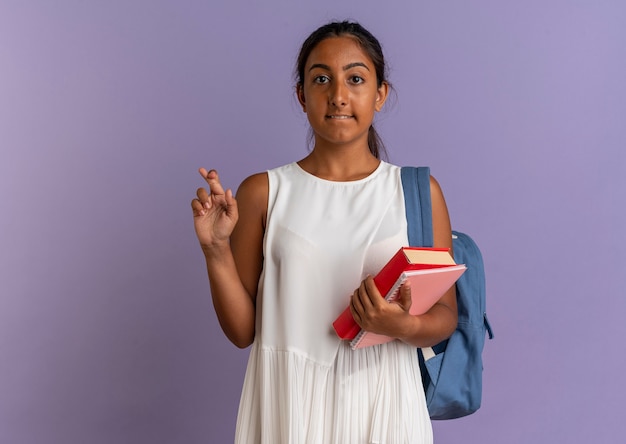 Betroffenes junges Schulmädchen, das Rucksack hält Buch mit Notizbuch hält und Finger kreuzt