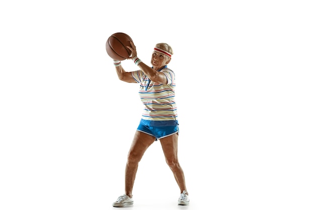 Bewegung. Ältere Frau, die Sportkleidung trägt, die Basketball auf weißem Hintergrund spielt. Das kaukasische weibliche Model in guter Form bleibt aktiv. Konzept von Sport, Aktivität, Bewegung, Wohlbefinden, Selbstvertrauen. Copyspace.