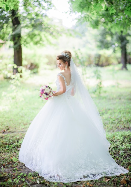 Bezaubernde Braut wirft mit buntem Hochzeitsblumenstrauß im Park auf